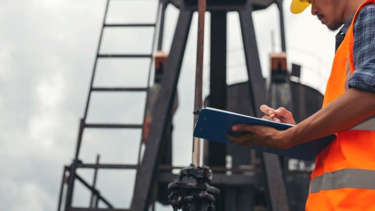 Workers standing and checking beside working oil pumps